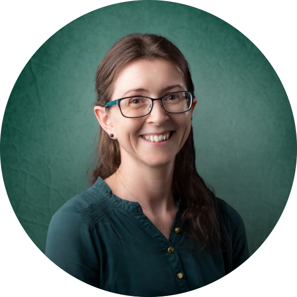 Joanne smiling with brown hair, glasses, and a forest-green shirt