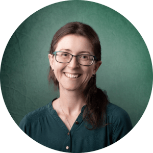 Joanne smiling with brown hair and glasses in a dark green shirt.
